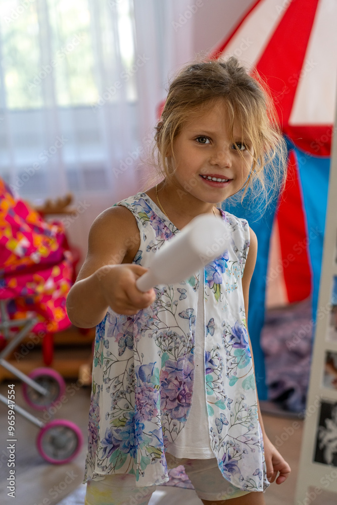 A young girl smiles while playfully holding a white object in a vibrant and colorful indoor playroom, illuminated by natural light