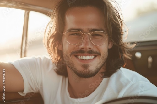 In a light and airy interior, a smiling man with glasses sits in a car looking back over the seat