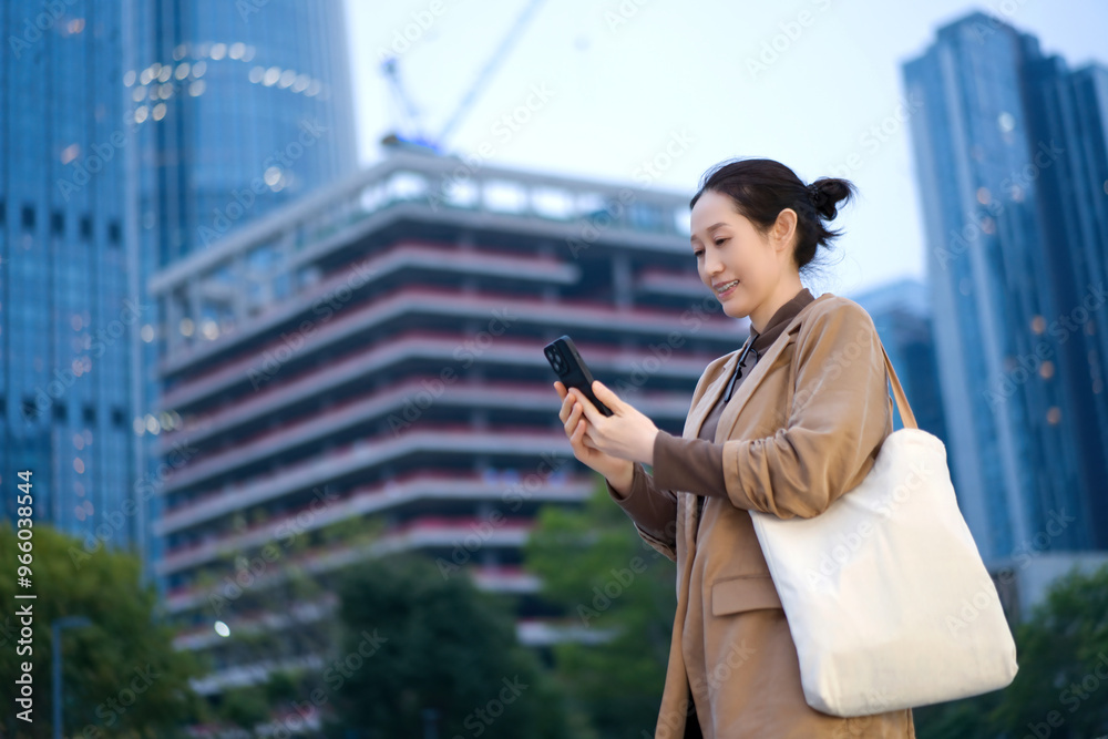 Fototapeta premium Young Woman Engaged with Smartphone in Modern Urban Landscape