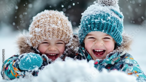 Two happy kids wearing colorful winter clothes and hats, laughing, and playing in the snow during a fun-filled snowy day outdoors. They are covered in snowflakes.