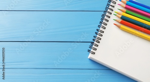 Colorful pencils arranged beside a blank notepad on a vibrant blue wooden tab...