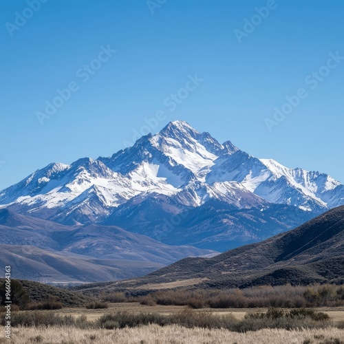 Snow-capped mountain peak with a clear blue sky and rolling hills.