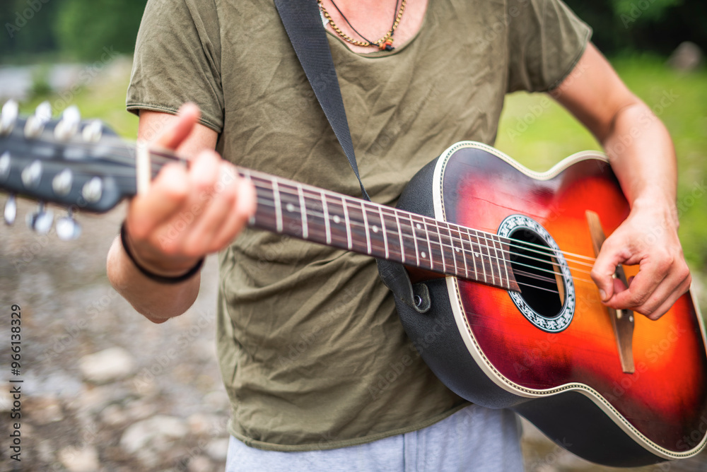 A young man plays the guitar against a natural backdrop.