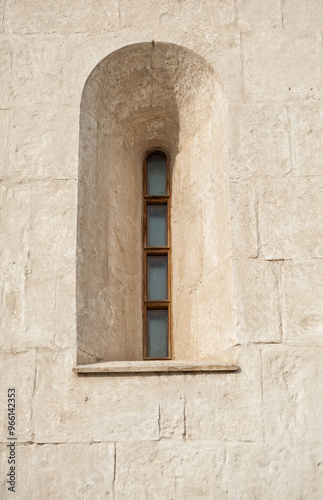 Narrow arched window in a weathered stone wall, evoking ancient architecture