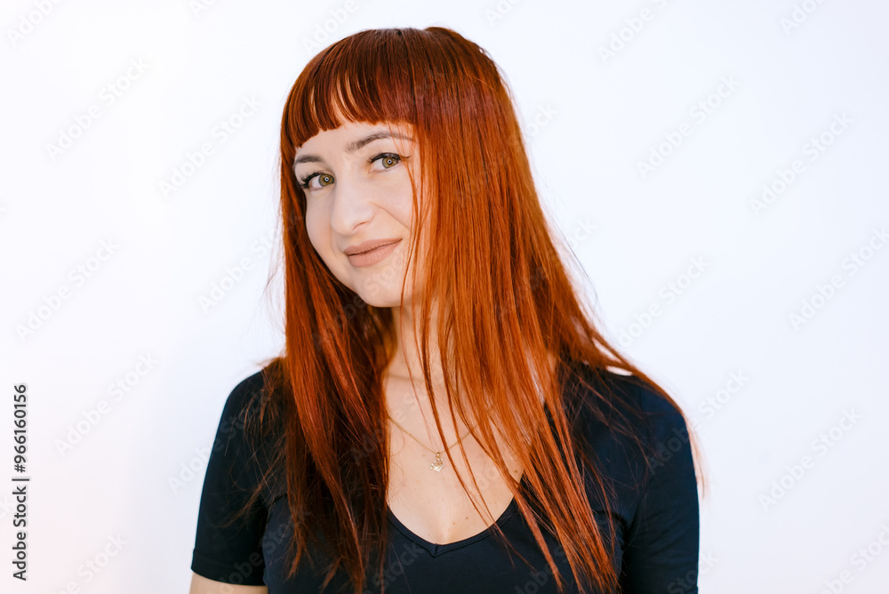 Young woman with long red hair smiling against a bright white backdrop. A young woman with vibrant red hair smiles playfully while standing Young woman with long red hair smiling against a bright white backdrop. A young woman with vibrant red hair smiles playfully while standing