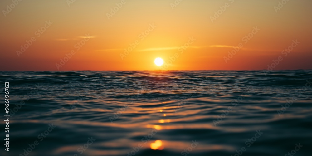 Obraz premium The sun is setting over the ocean, casting a warm glow on the water. The sky is a mix of orange and pink hues, creating a serene and peaceful atmosphere. The water is calm and still