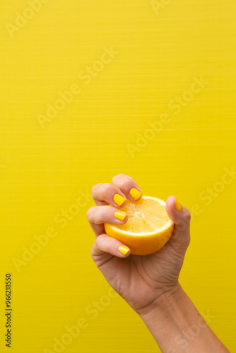 A woman's hand with yellow fingernails squeezing half a lemon