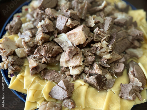 The cooked meat and pieces of dough are on a plate. The traditional meatmeal dish of the Turkic peoples called beshbarmak is shown in close-up.  photo