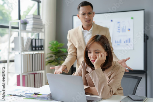 Businessman angrily criticizing a female colleague working on laptop in the office photo