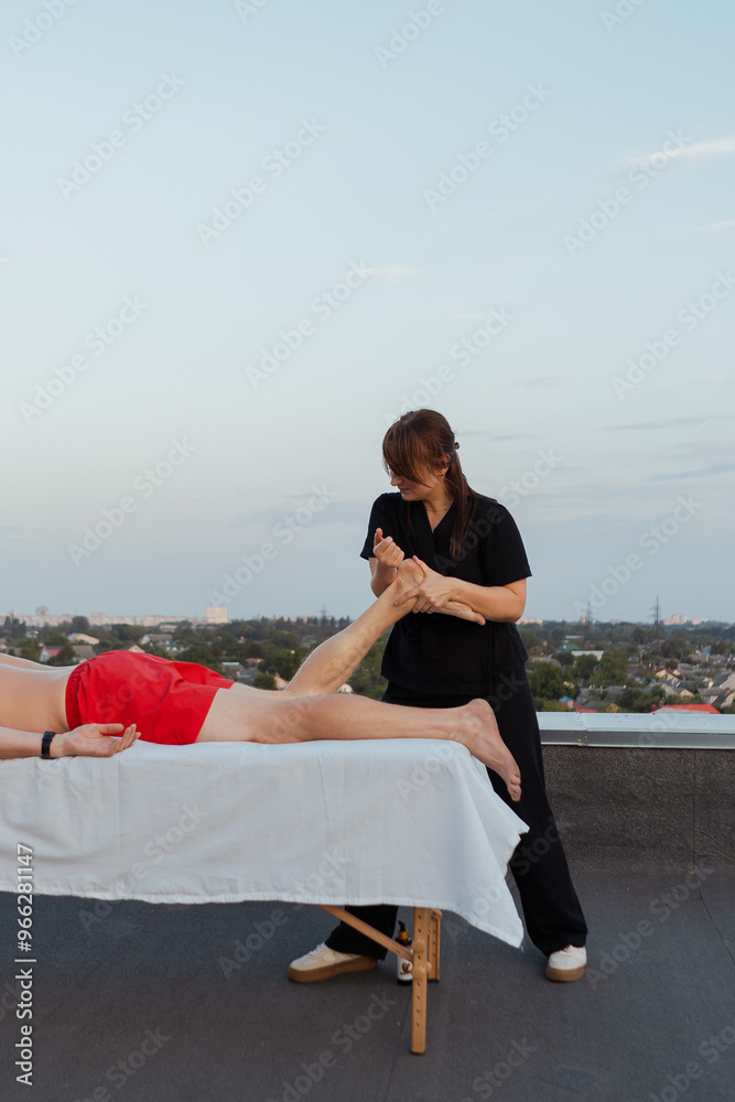 Master massage therapist on the roof of a house in the city gives a massage to a beautiful young man with a tattoo, close-up hands lubricating skin and body with oil. Medicine and procedure Master massage therapist on the roof of a house in the city gives a massage to a beautiful young man with a tattoo, close-up hands lubricating skin and body with oil. Medicine and procedure