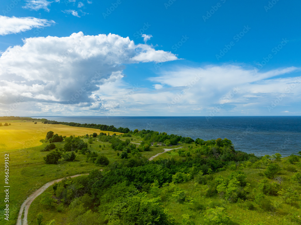 Aerial view of calm and wild Saka beach with a clear blue water on a cloudy summer day. Beautiful yellow and green fields and countryside road. Saka, Ida Viru county, Estonia. Selective focus. Aerial view of calm and wild Saka beach with a clear blue water on a cloudy summer day. Beautiful yellow and green fields and countryside road. Saka, Ida Viru county, Estonia. Selective focus.