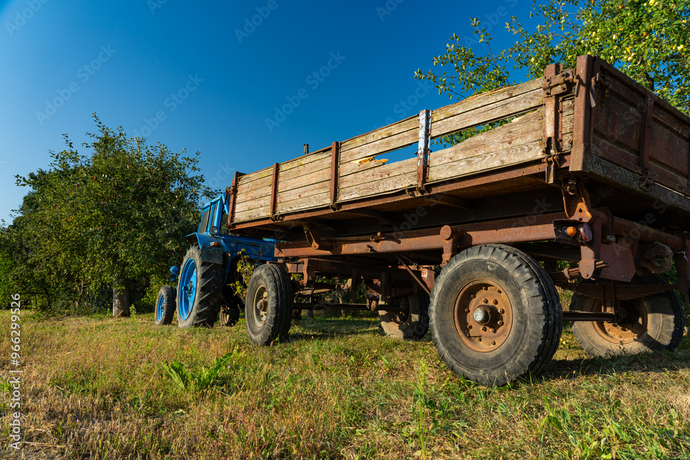 Obraz premium A blue, old tractor with a trailer stands near a field in the village. Morning