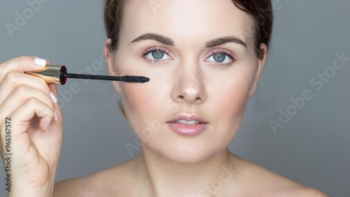 Close-up portrait of young woman on gray background, doing makeup. Mascara for eyelashes. Self care.