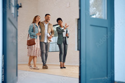 Happy African American real estate agent showing  house for sale to couple interested in buying it. Copy space.