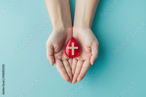 Top view photo of a female hands holding blood droplet with cross sign on palms on pastel blue background.