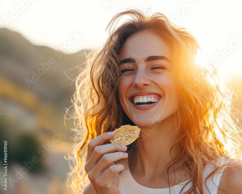 Woman with curly hair smiling as she holds a small snack in the sunshine