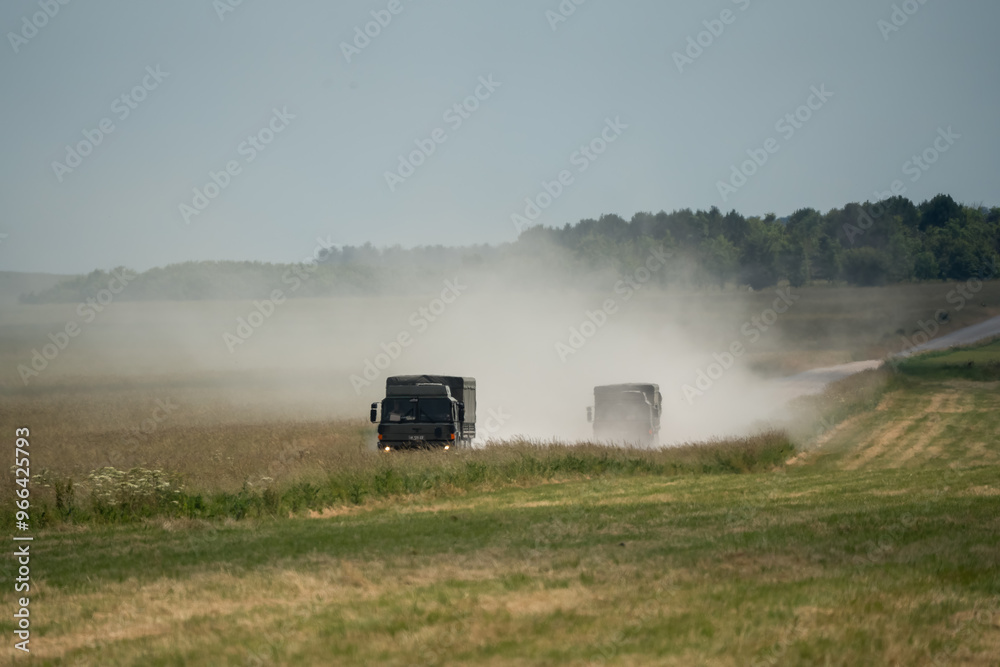 Fototapeta premium a pair of British army MAN SV4x4 utility trucks creating a dust cloud on an unmade road