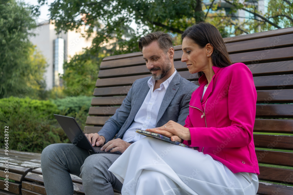 Businessman and woman using laptop while working at bench in the city park. Businessman and woman using laptop while working at bench in the city park.