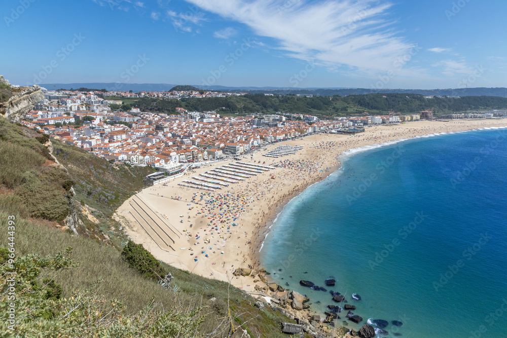 Nazaré sand beach and hills on a summer day with a beach full of people at Nazare Portugal. Nazaré sand beach and hills on a summer day with a beach full of people at Nazare Portugal.