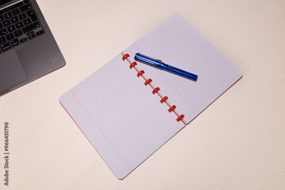 An overhead shot of an open notebook with a blue fountain pen and part of a laptop on a clean, light-colored desk. An overhead shot of an open notebook with a blue fountain pen and part of a laptop on a clean, light-colored desk.