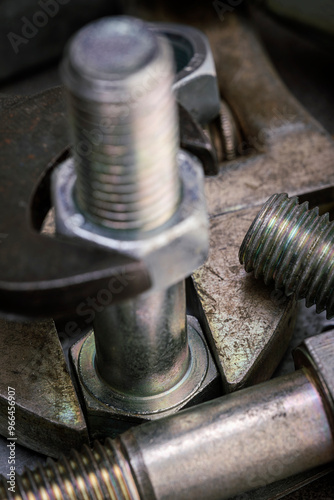 Wrench tightening metal bolt surrounded by nuts and bolts. Macro shot of construction and repair tools.