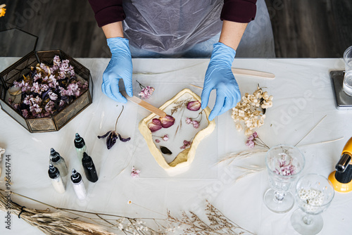 Hands arranging pressed flowers into resin frame, showcasing traditional crafts in modern DIY home decor. Eco-friendly, sustainable crafting techniques.