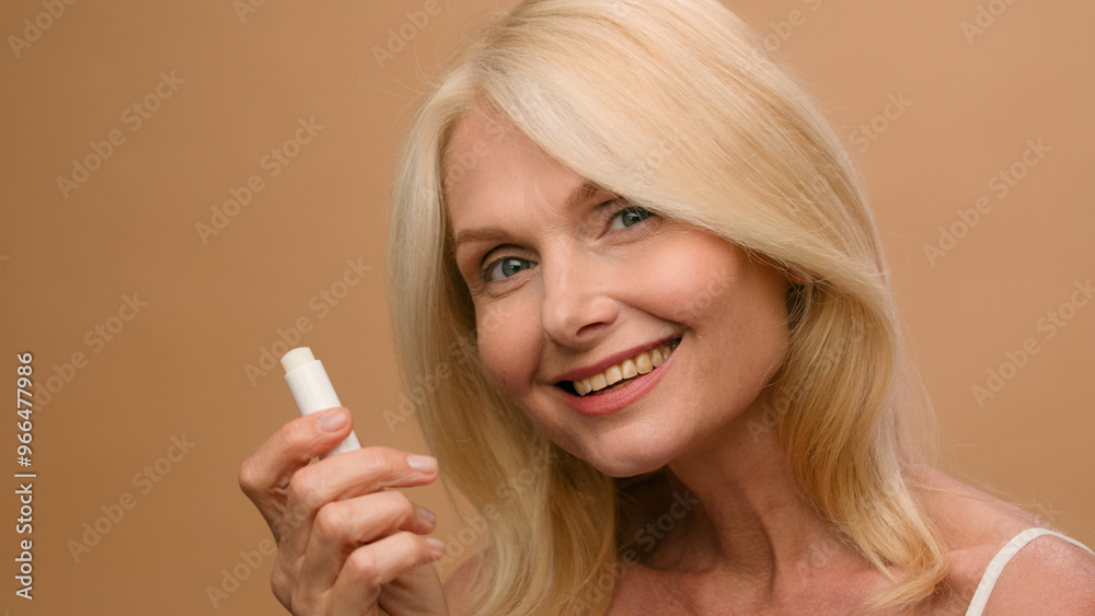 Mature middle-aged elderly woman model makeup hygienic lipstick applying moisturizing lip balsam natural beauty face skin care anti-aging cosmetic flirty senior lady smiling on beige studio background Mature middle-aged elderly woman model makeup hygienic lipstick applying moisturizing lip balsam natural beauty face skin care anti-aging cosmetic flirty senior lady smiling on beige studio background