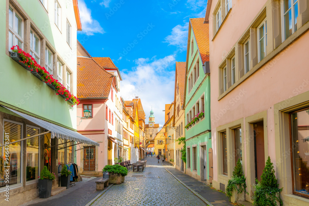 Fototapeta premium A medieval cobblestone street leads to the 12th century Markusturm Markus Tower, one of the original arched town fortress gates in the historic village of Rothenburg ob der Tauber Germany.