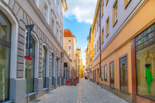 A narrow cobblestone alley of colorful buildings with shops and sidewalk cafes in the Altstadt old town district of the Bavarian city of Regensburg, Germany.