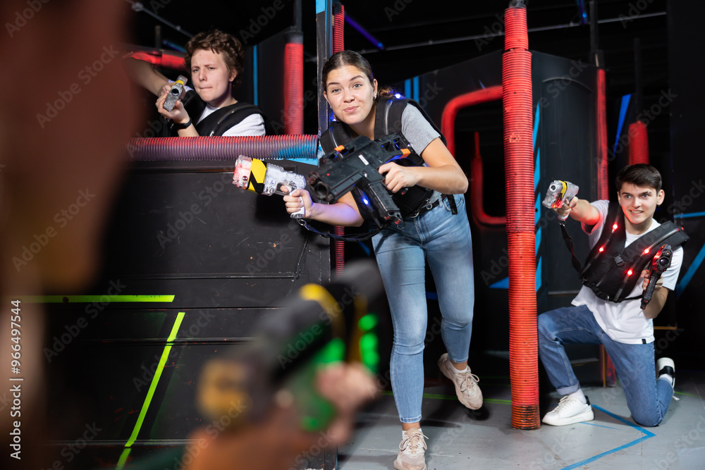 Fototapeta premium Laughing players young mens and womens playing in teams in dark laser tag station