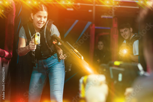 Smiling girl with laser pistol during playing laser tag with her friends in dark room