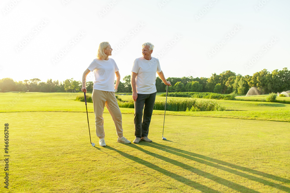 old senior couple in white clothes playing golf on golf course and chatting at sunset, elderly man and woman actively relaxing outdoors and laughing, pensioners on vacation old senior couple in white clothes playing golf on golf course and chatting at sunset, elderly man and woman actively relaxing outdoors and laughing, pensioners on vacation