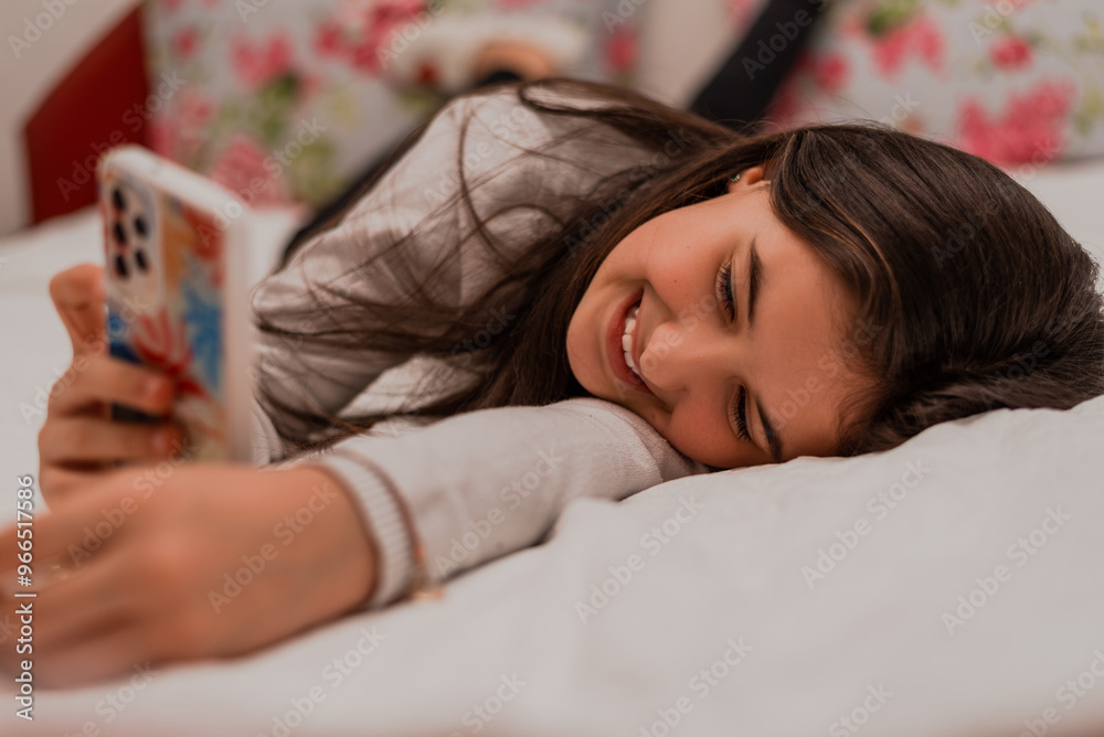 A smiling teenage girl using a phone while comfortable lying on the bed at home. A smiling teenage girl using a phone while comfortable lying on the bed at home.