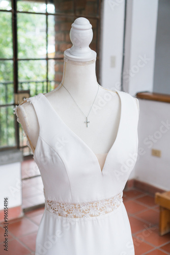 Silver cross necklace displayed on mannequin wearing white wedding dress. Religious wedding details. photo