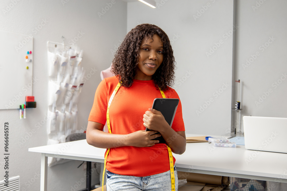 Woman tailor holding tablet with measuring tape around neck in well-equipped atelier Woman tailor holding tablet with measuring tape around neck in well-equipped atelier