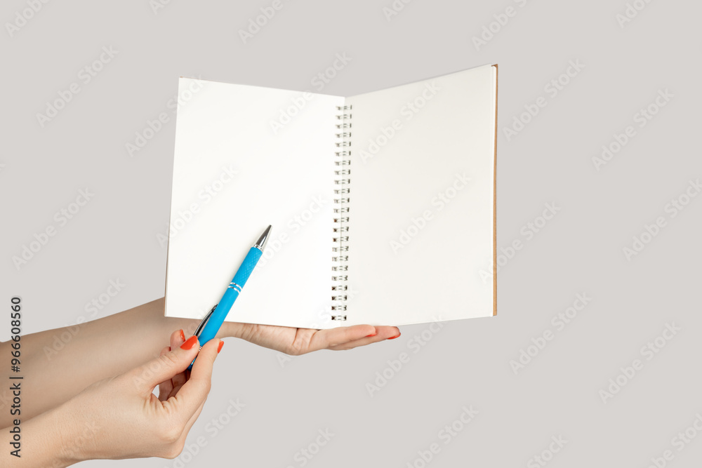Closeup of woman hand showing open notebook with empty pages, pointing at something with pen, copy space. Indoor studio shot isolated on gray background. Closeup of woman hand showing open notebook with empty pages, pointing at something with pen, copy space. Indoor studio shot isolated on gray background.