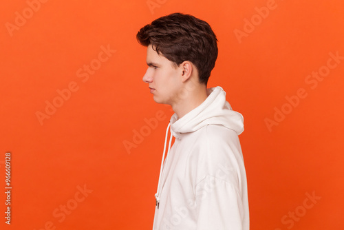 Portrait of serious assertive handsome young man wearing white hoodie standing looking forward, being confident and attentive. Indoor studio shot isolated on orange background.