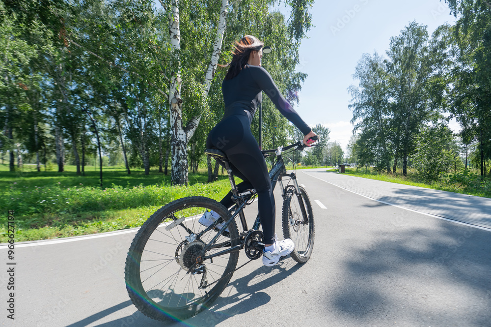 Rear view of Caucasian woman riding bike in park. Rear view of Caucasian woman riding bike in park.