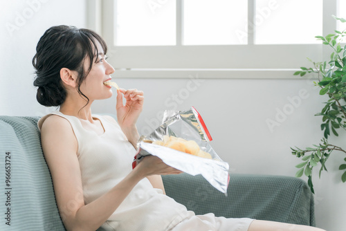 Foto 自宅のソファでポテトチップスを食べる若いアジア人女性（暴飲暴食・間食・高カロリー）