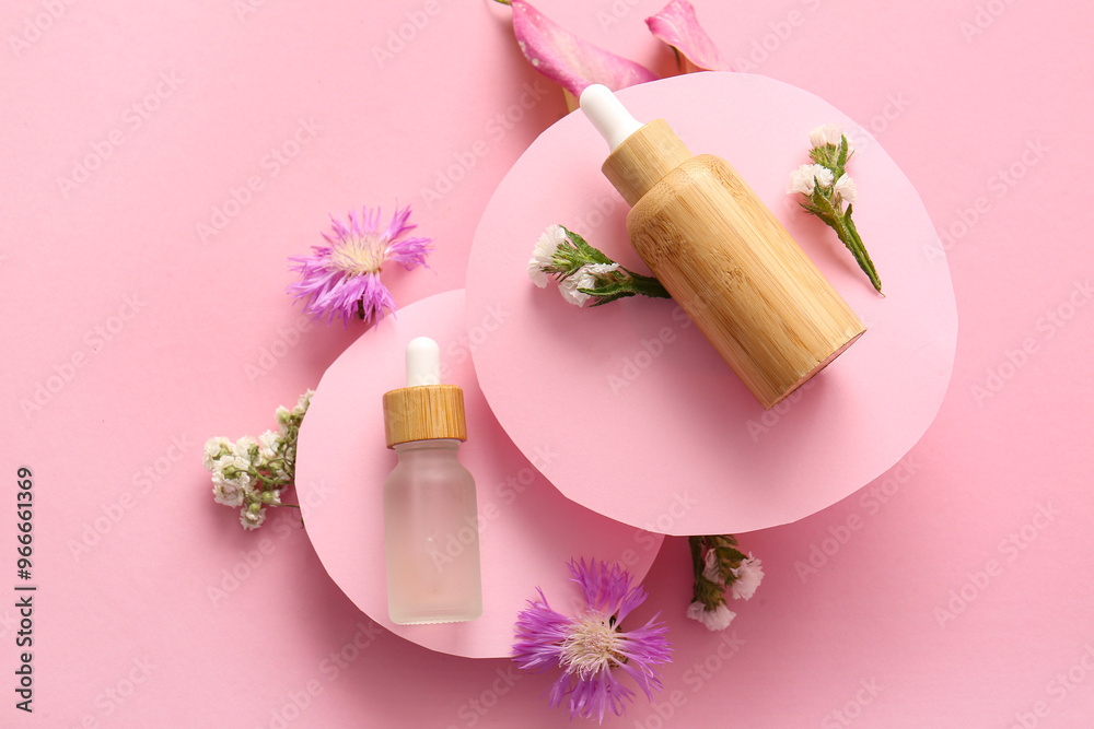 Composition with bottles of essential oil and beautiful flowers on pink background Composition with bottles of essential oil and beautiful flowers on pink background