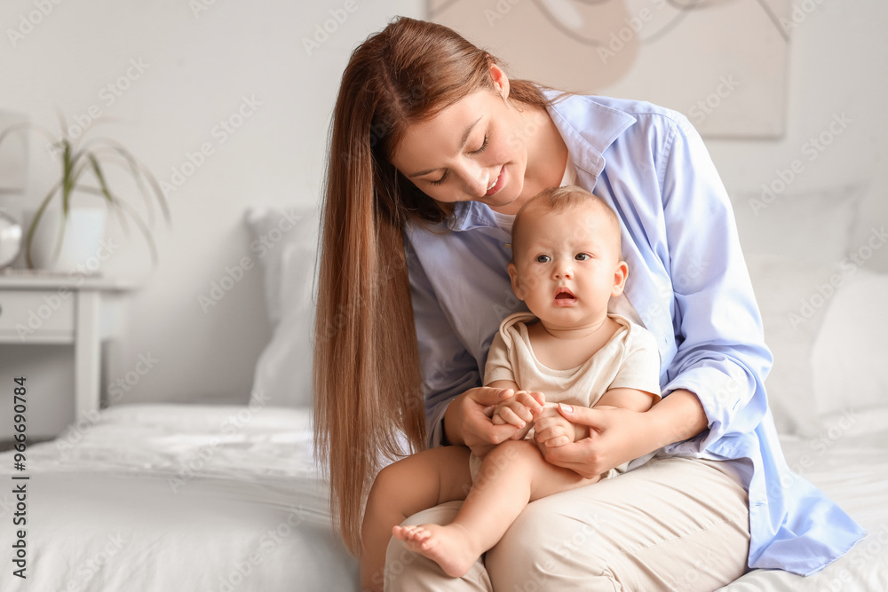 Beautiful young happy mother with cute little baby sitting in bedroom at home Beautiful young happy mother with cute little baby sitting in bedroom at home