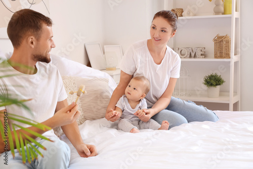 Happy young couple with cute little baby and rattle sitting on bed at home