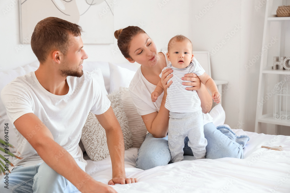 Fototapeta premium Happy young couple with cute little baby sitting on bed at home