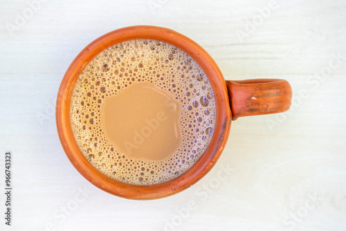 A cup of hot milk tea or dudh cha in a traditional clay cup. Top view of doodh chai in an earthenware cup on a light wooden surface. photo