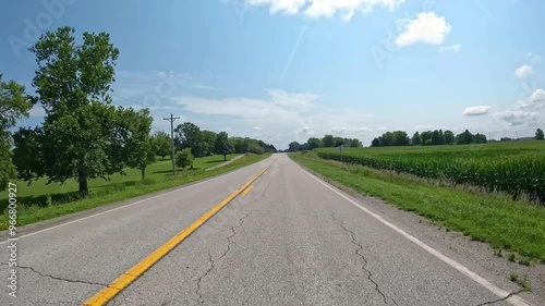 POV - driving on a rural county road past trees and lush, green fields in late summer in central Iowa; concepts of farming and rural life photo