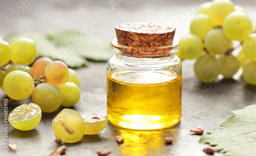 Grape seed oil in glass bottle with grapes, seeds and leaves close on black background, closeup, healthy food and natural skin and body treatment and care concept