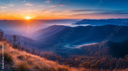 Witness the beauty of a mountain range as the sun rises over the horizon, illuminating the landscape with warm light while mist settles in the valleys below