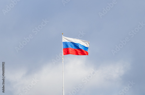 Russian tricolor flag waving in the wind against a blue sky.