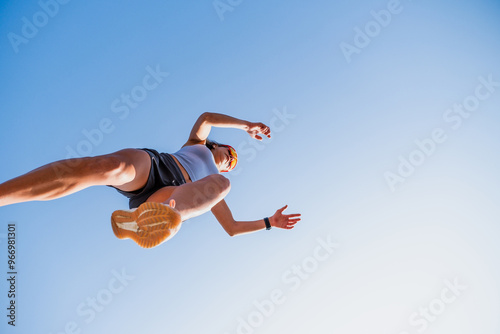 Young female athlete leaps over a hurdle in a parkour workout under a clear blue sky