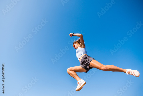 Young female athlete leaps over a hurdle in a parkour workout under a clear blue sky